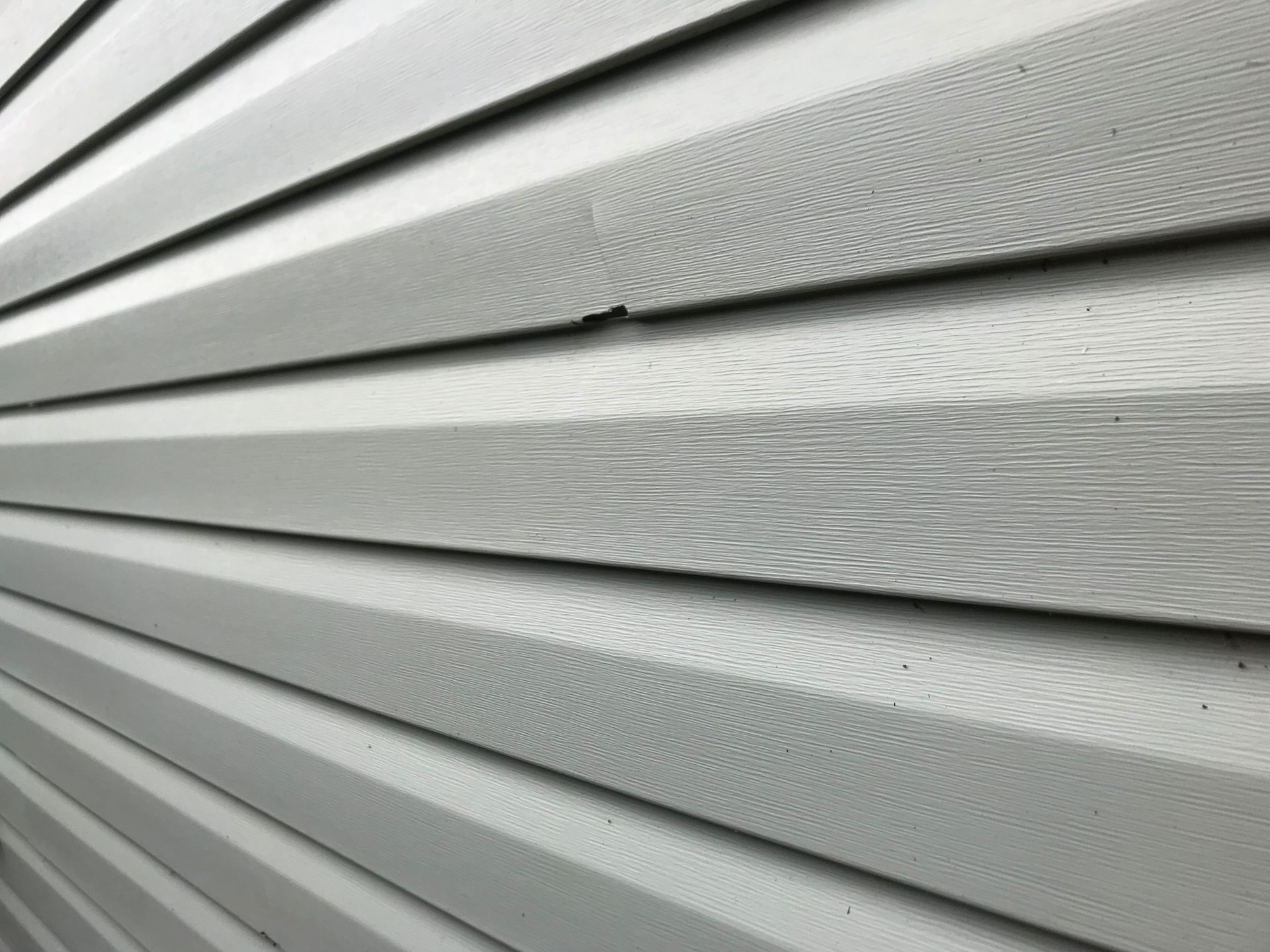 Close-up of light gray vinyl siding with horizontal panels and textured surface