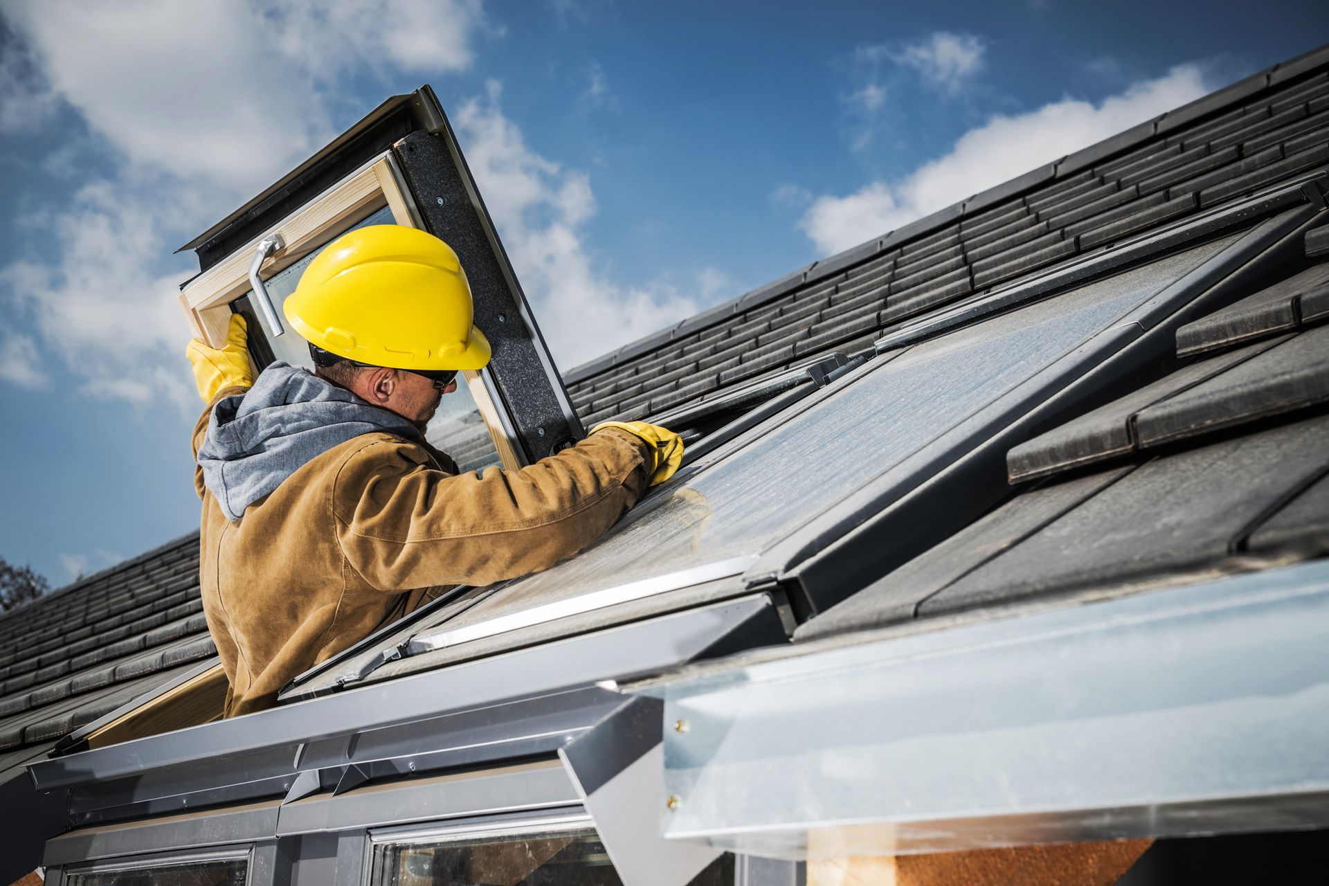 Worker in a yellow hard hat installing solar panels on a rooftop under a blue sky