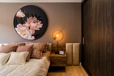Modern bedroom with floral wall art, warm lamp, and beige bedding on wood floor