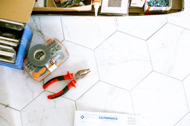 Tools and pliers on a white tiled floor beside a tape measure and organizer box