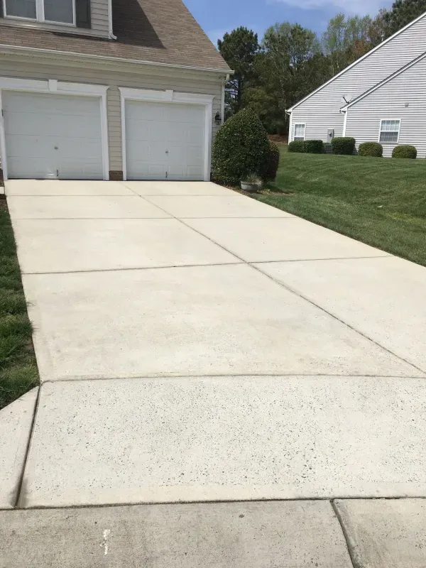 A concrete driveway leading to a house with two garage doors.