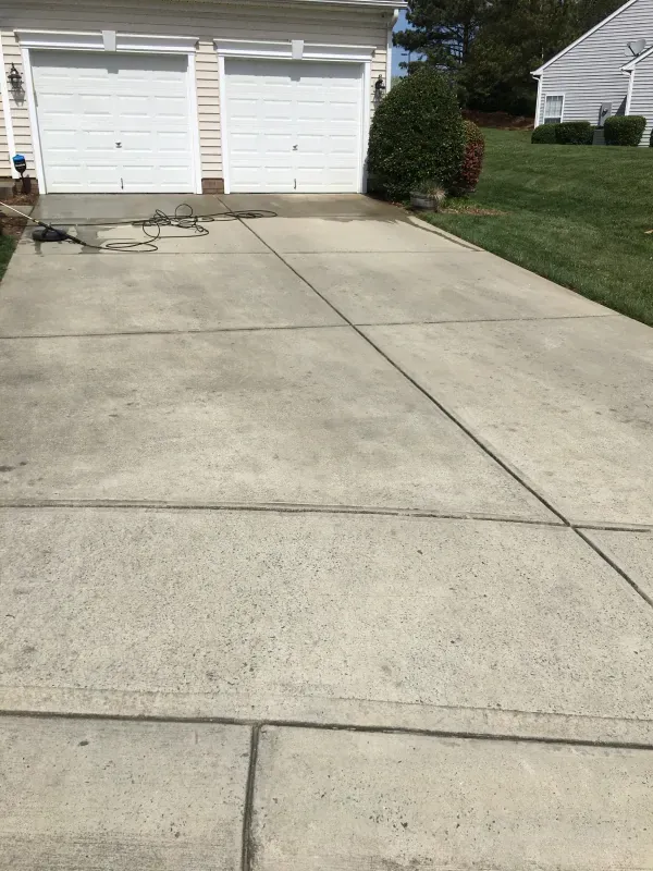 A concrete driveway leading to a house with two garage doors.
