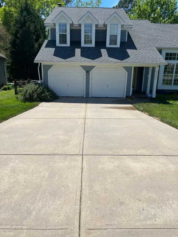 A concrete driveway leading to a house with two garage doors.