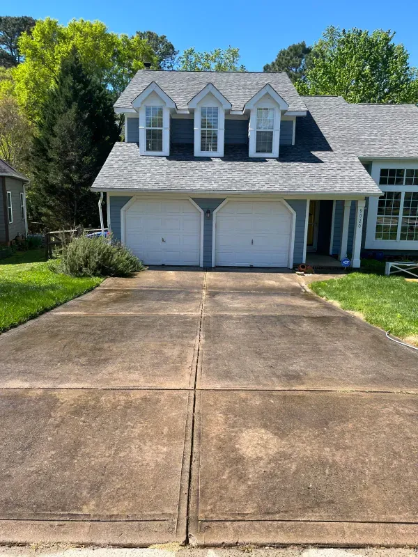 A house with two garage doors and a concrete driveway in front of it.