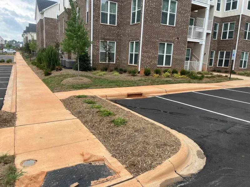 A brick building with a sidewalk and a parking lot in front of it.