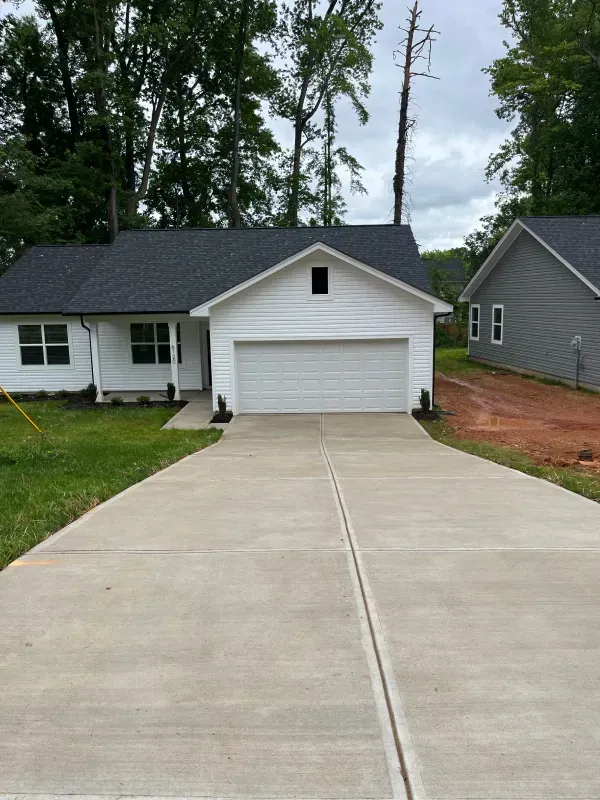 A concrete driveway leading to a white house with a garage.