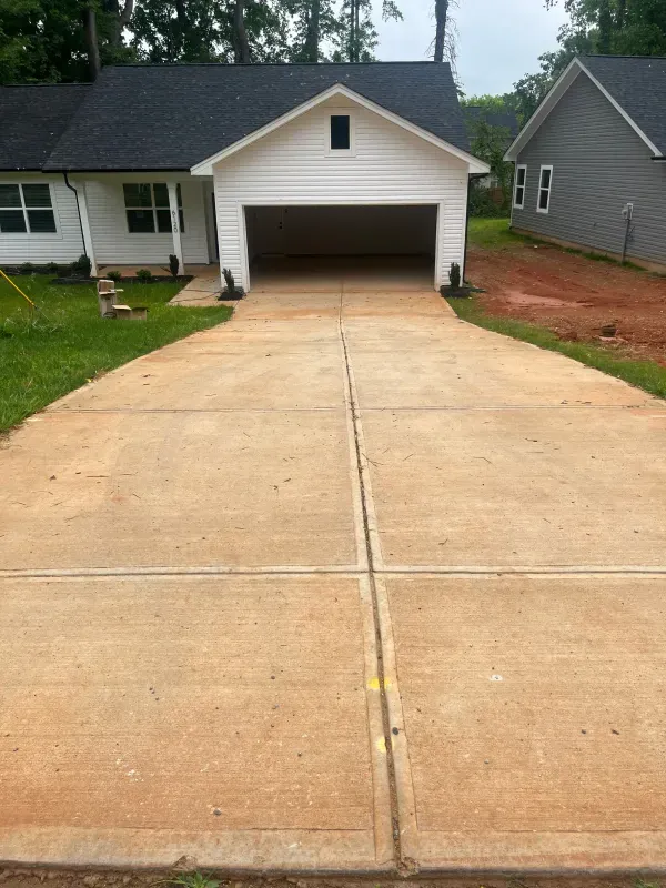 A concrete driveway leading to a white house with a garage.