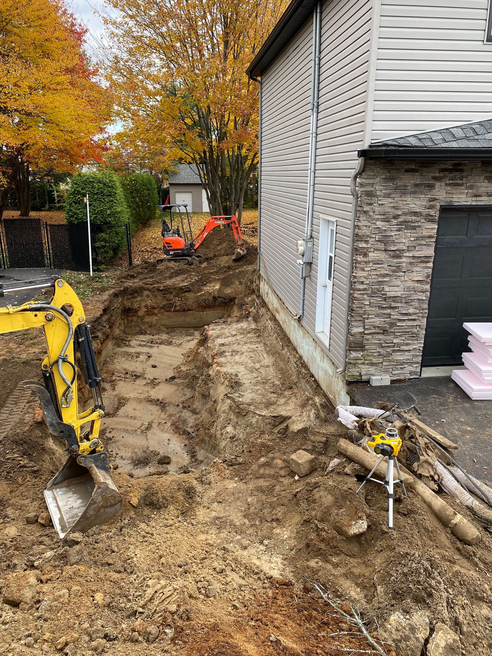 Une excavatrice jaune creuse un trou devant une maison.