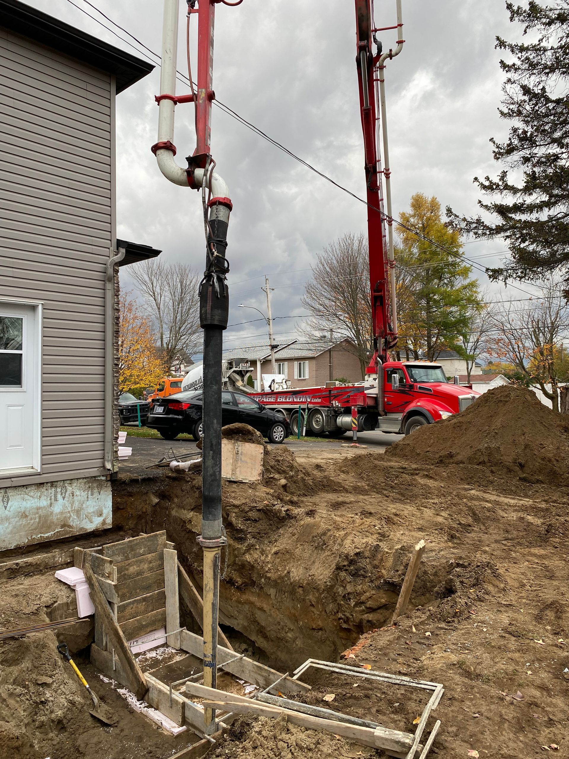 Un camion rouge pompe du béton dans un trou devant une maison.