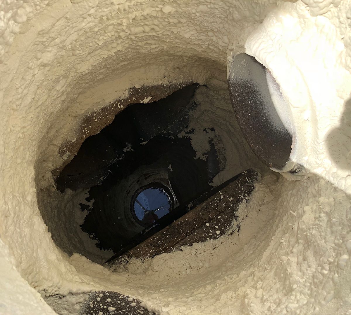 Looking down a deep dirt well with dark water at the bottom and a white bucket-like object on the right