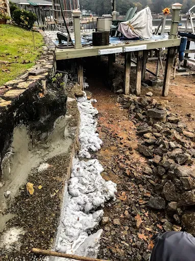 Eroded dirt trench beside a concrete slab, with white foam or concrete runoff along the left edge.