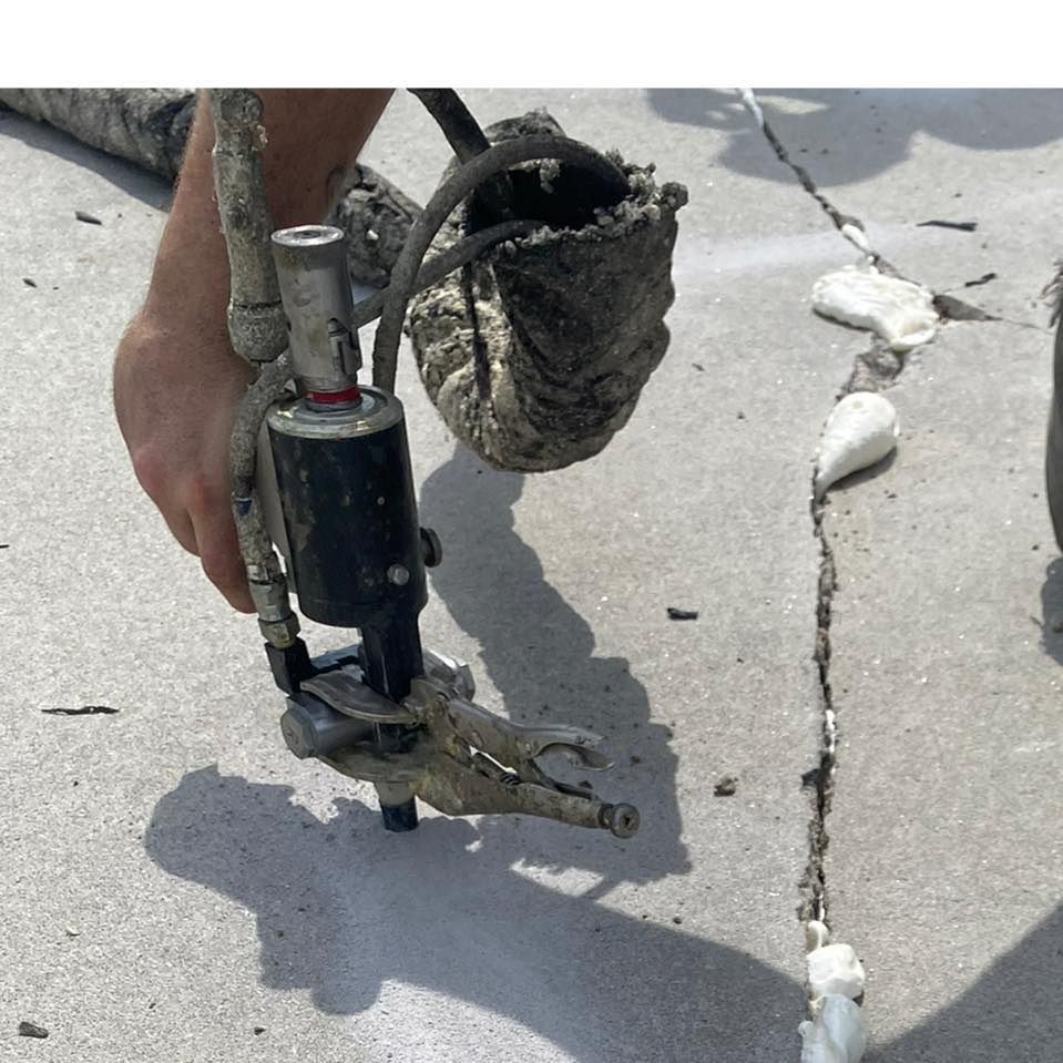 A hand-held metal tool applying sealant to a cracked concrete sidewalk