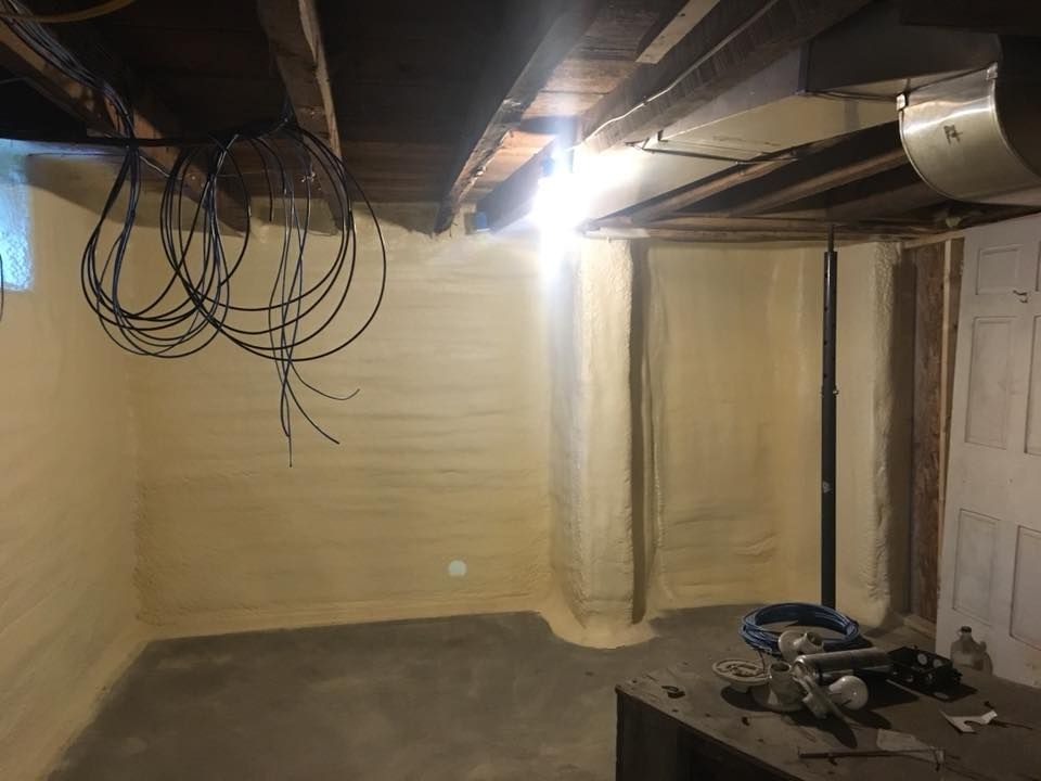 Unfinished basement room with exposed beams, hanging wires, beige walls, and a miter saw on the floor.