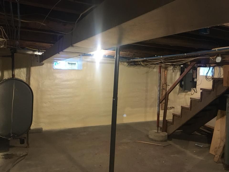 Empty basement with concrete floor, exposed beams, and a staircase on the right.