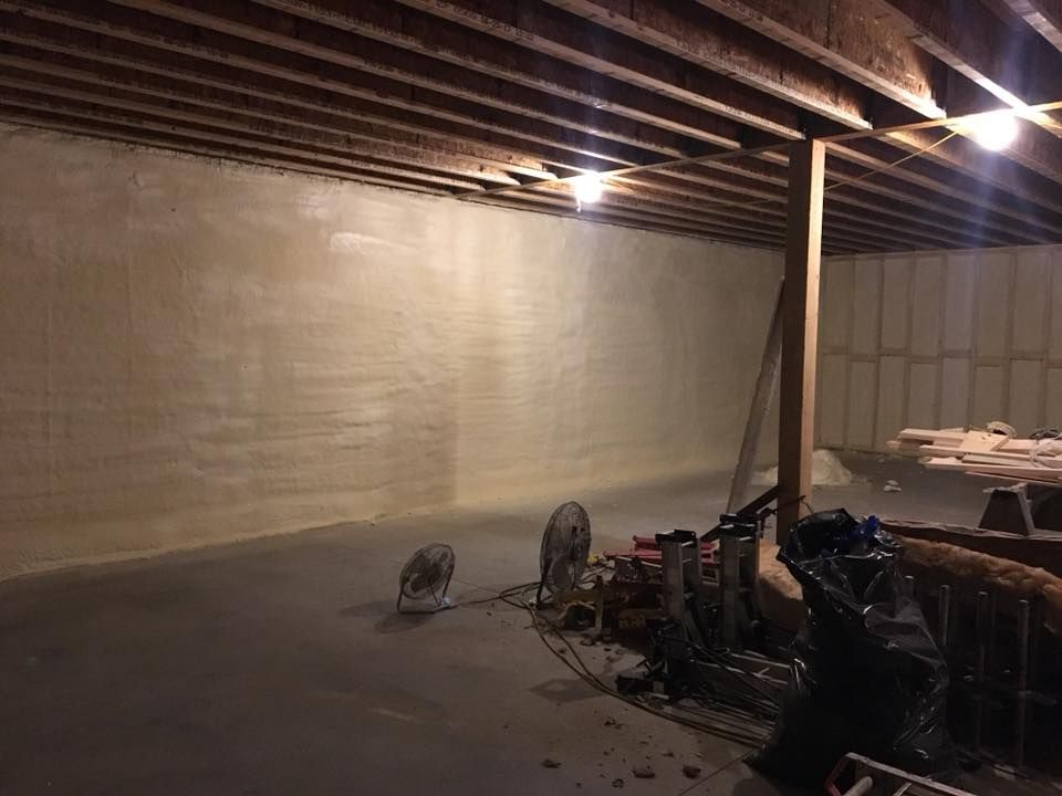 Dim unfinished basement with concrete walls, exposed ceiling beams, work lights, and construction tools on the floor