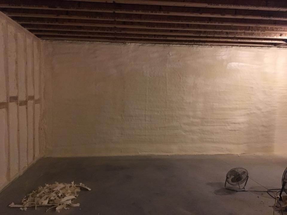 Empty basement with exposed wooden ceiling, concrete floor, and a small pile of debris near the wall.