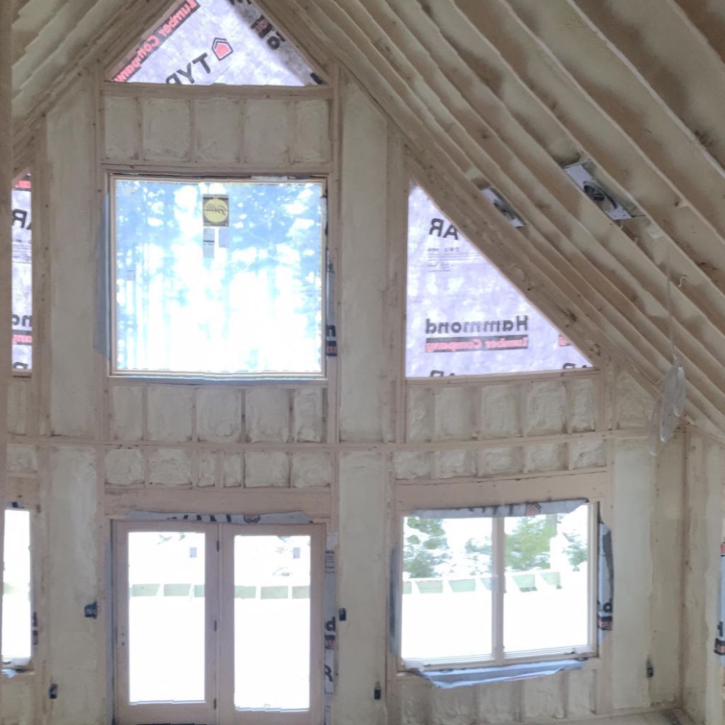 Interior of an unfinished house with exposed rafters and multiple window openings overlooking trees