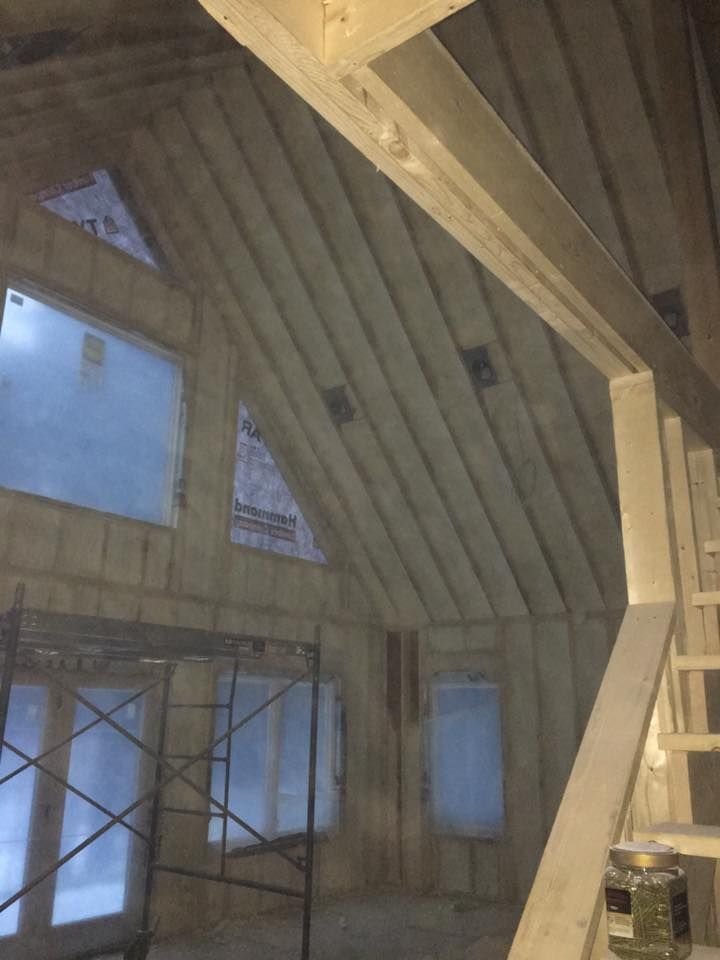 Wood-framed interior with exposed beams, slanted ceiling, windows, and insulation panels under construction
