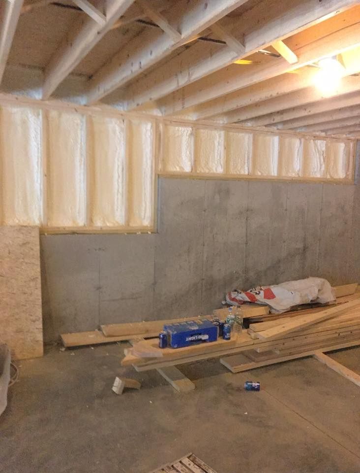 Basement under construction with exposed beams, insulated walls, and lumber on the floor