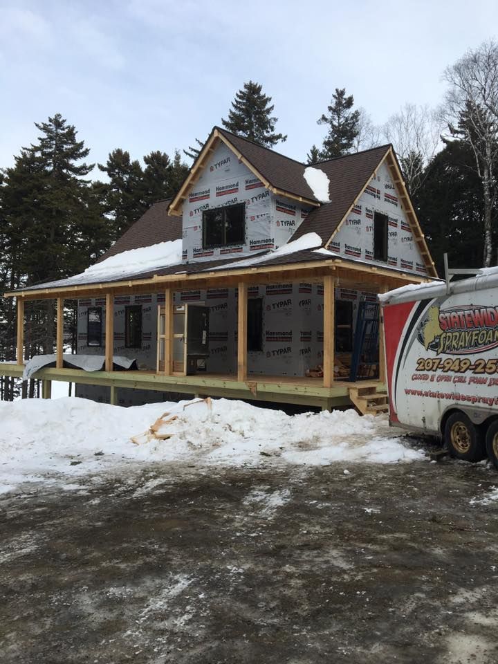 Snow-covered house under construction with a porch, viewed beside a parked work van in winter.