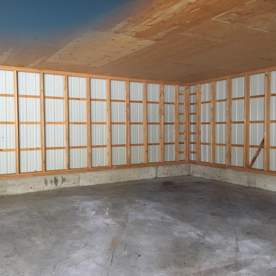 Empty unfinished room with concrete floor, exposed wood framing, and corrugated wall panels