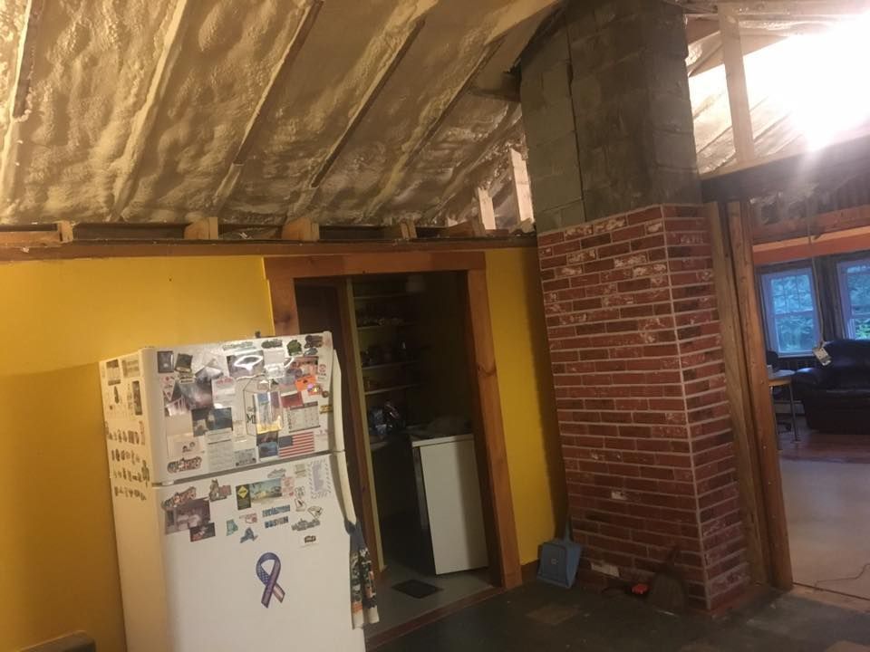 Interior room with exposed insulation ceiling, brick wall, and a refrigerator near a doorway
