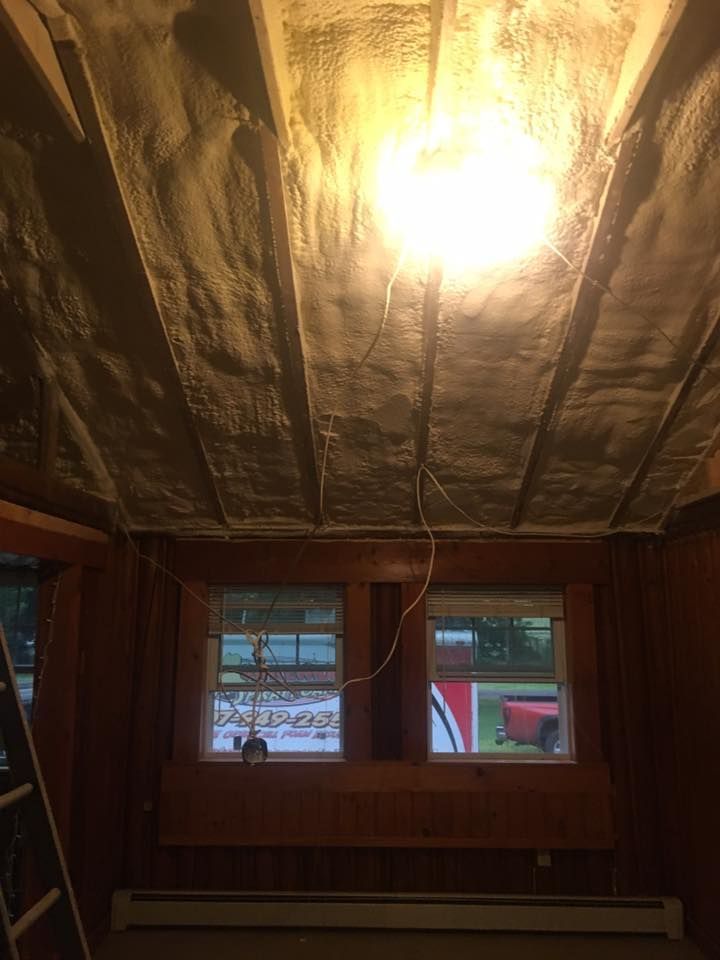 Dim unfinished room with exposed ceiling, bright hanging bulb, and two windows showing parked vehicles outside.