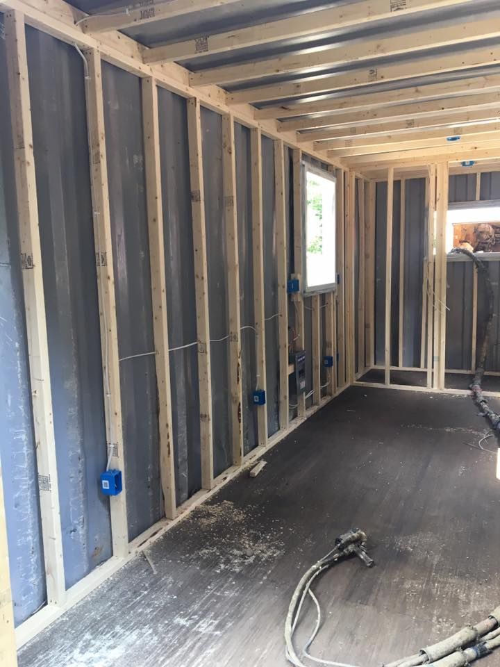 Unfinished room framing with exposed wooden studs, blue electrical boxes, and a window on the right.