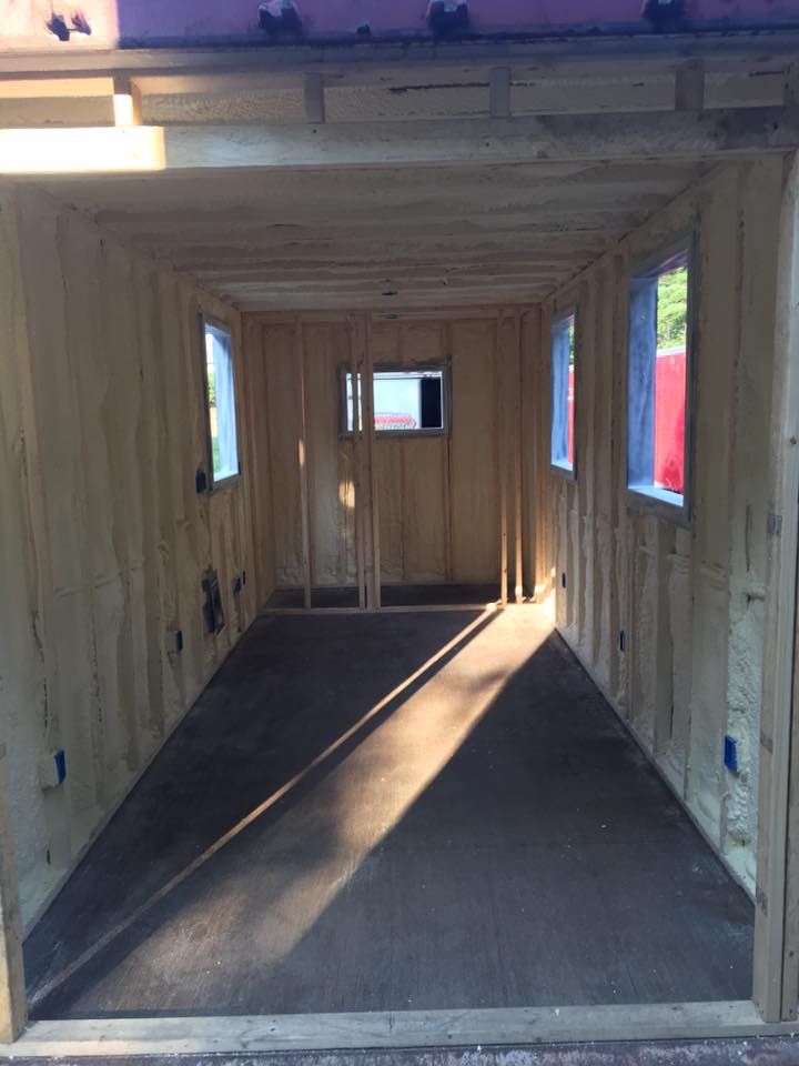 Inside a narrow wooden shed or trailer interior with windows and a dark floor under construction