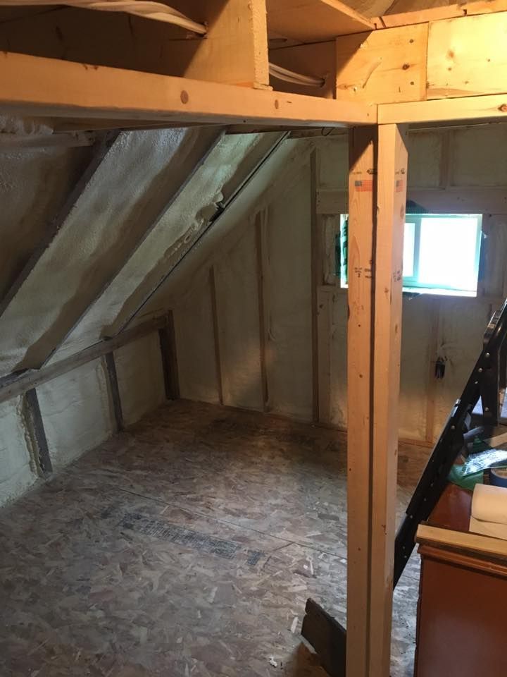 Small unfinished attic room with exposed wood framing, slanted ceiling, and two windows.
