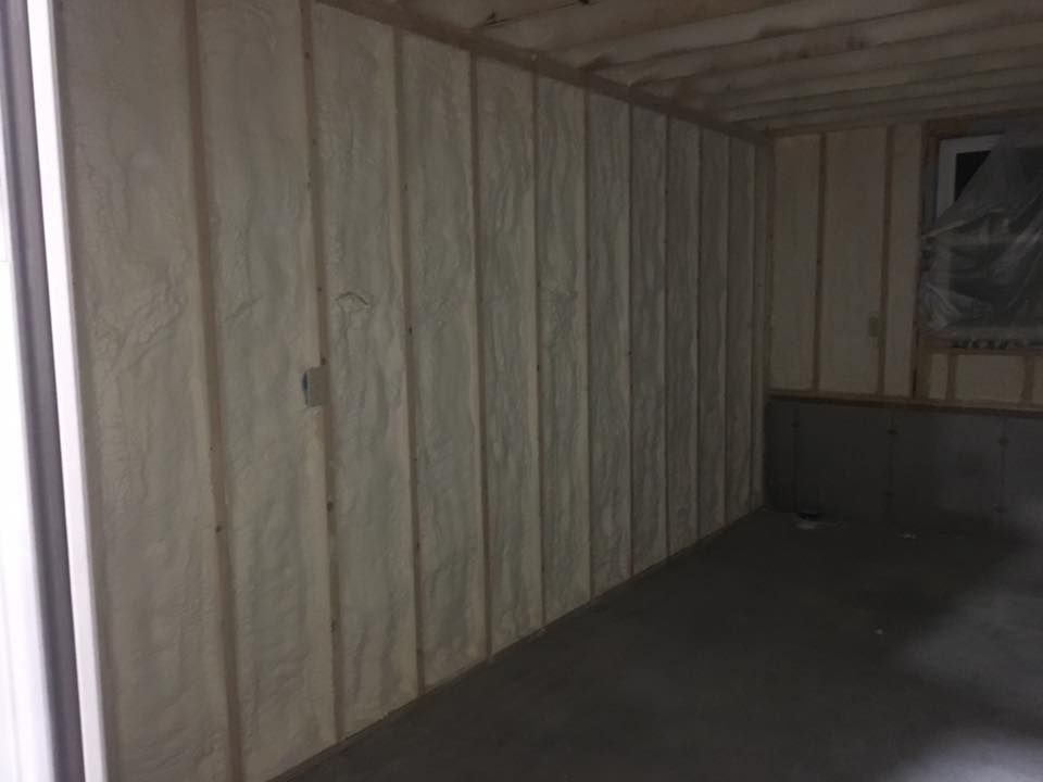 Empty unfinished room with exposed insulation, wood framing, and a dark floor.