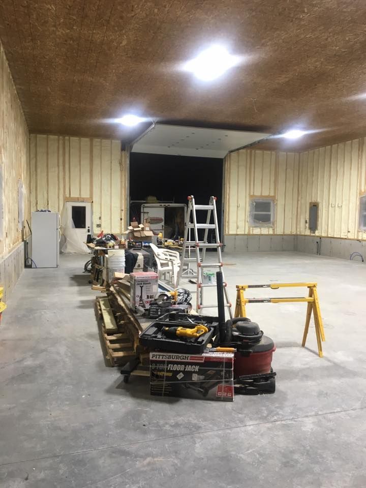 Empty warehouse with work tables, ladders, tools, and construction supplies on a concrete floor.