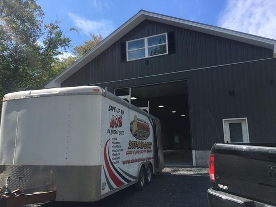 White box truck parked outside a dark gray auto shop with an open bay door.