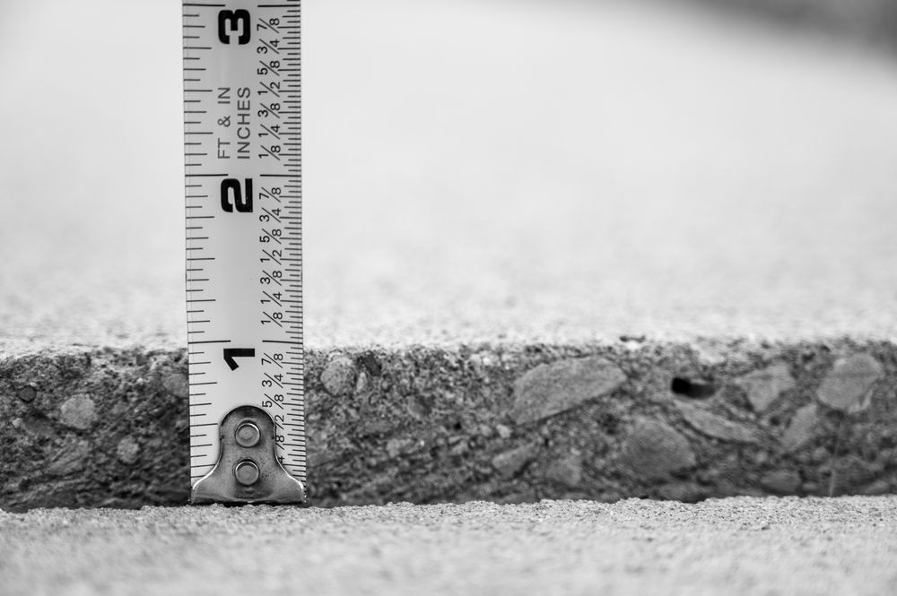 Measuring tape beside a rough concrete slab cross-section, showing its thickness.