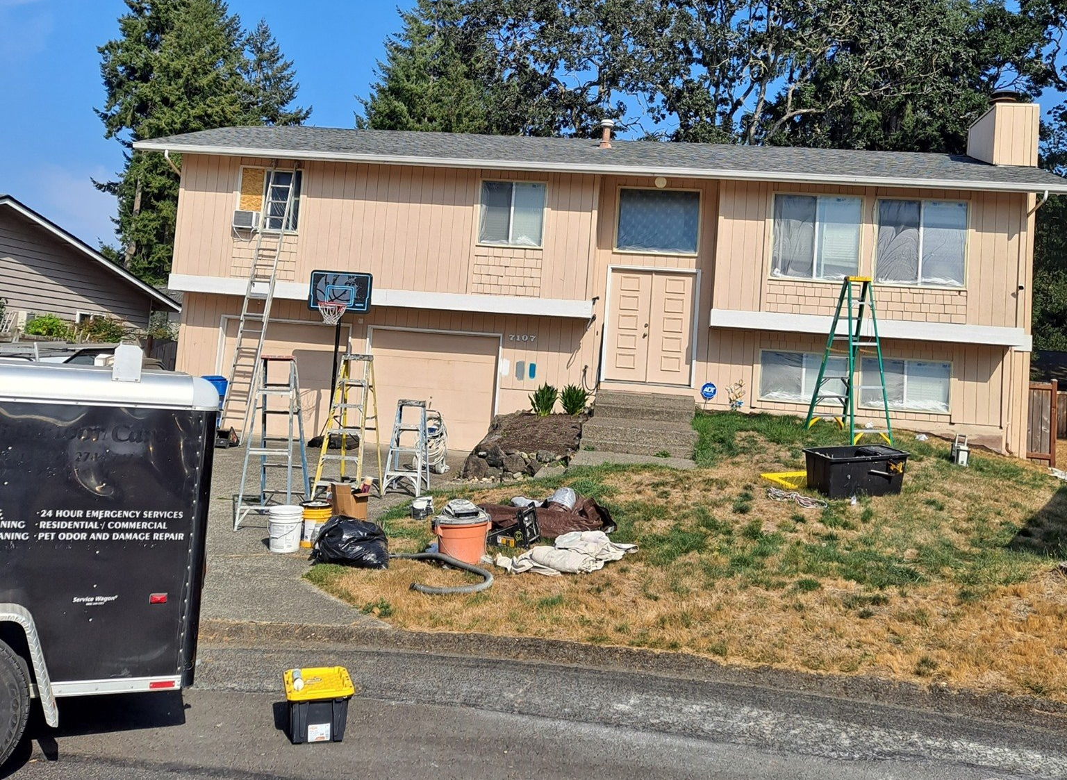 Ladders, various equipment, and a work trailer sit outside of a home as the crew prepares the exterior for new paint. 