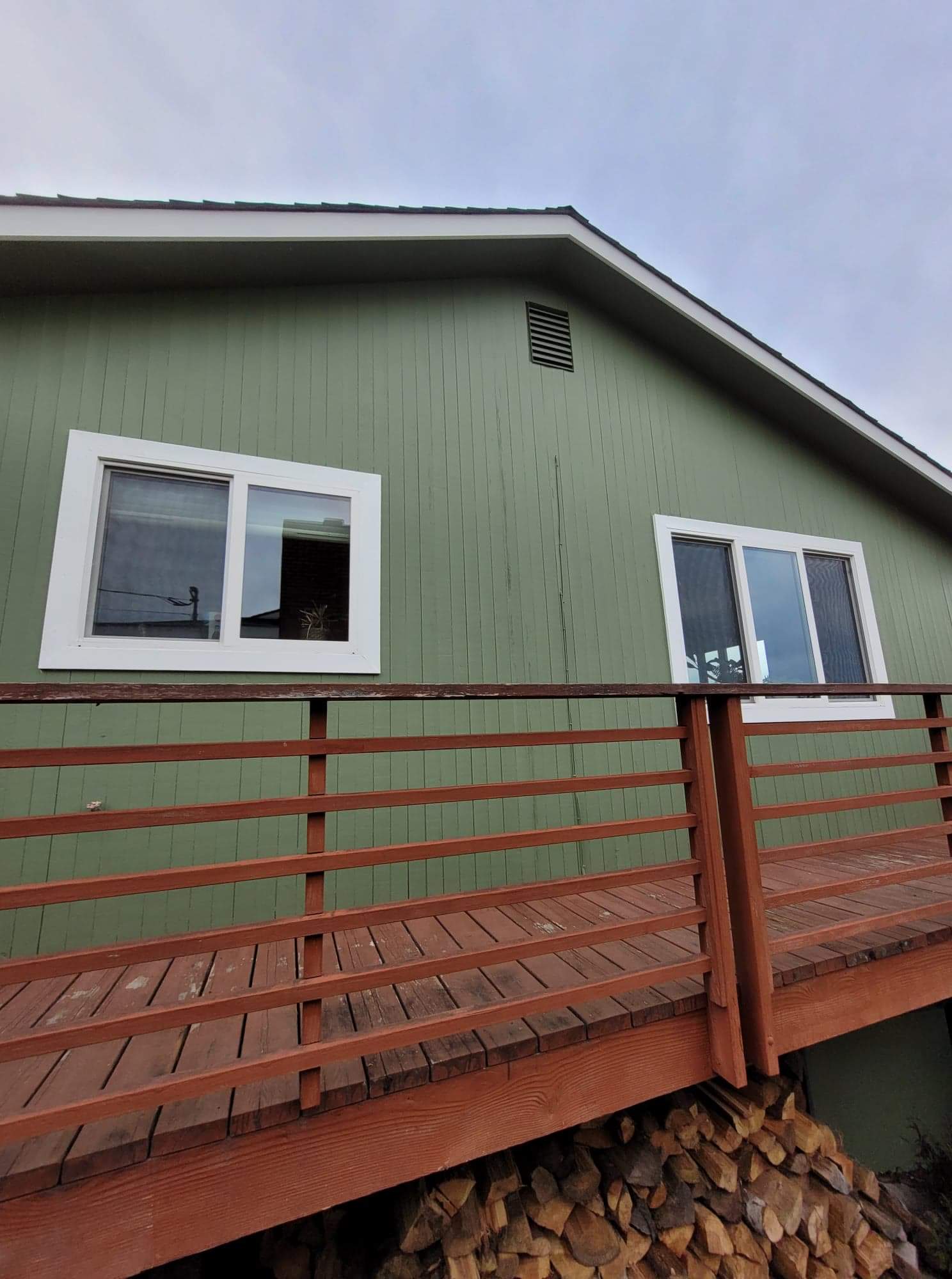 Green house exterior with white-framed windows and a red wooden deck railing.
