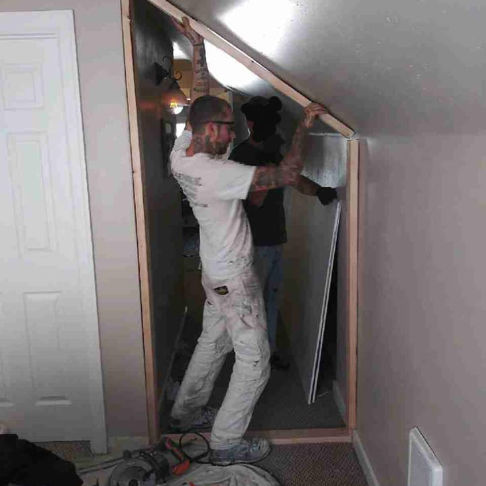 A contractor installs a drywall panel next to a small indoor closet.