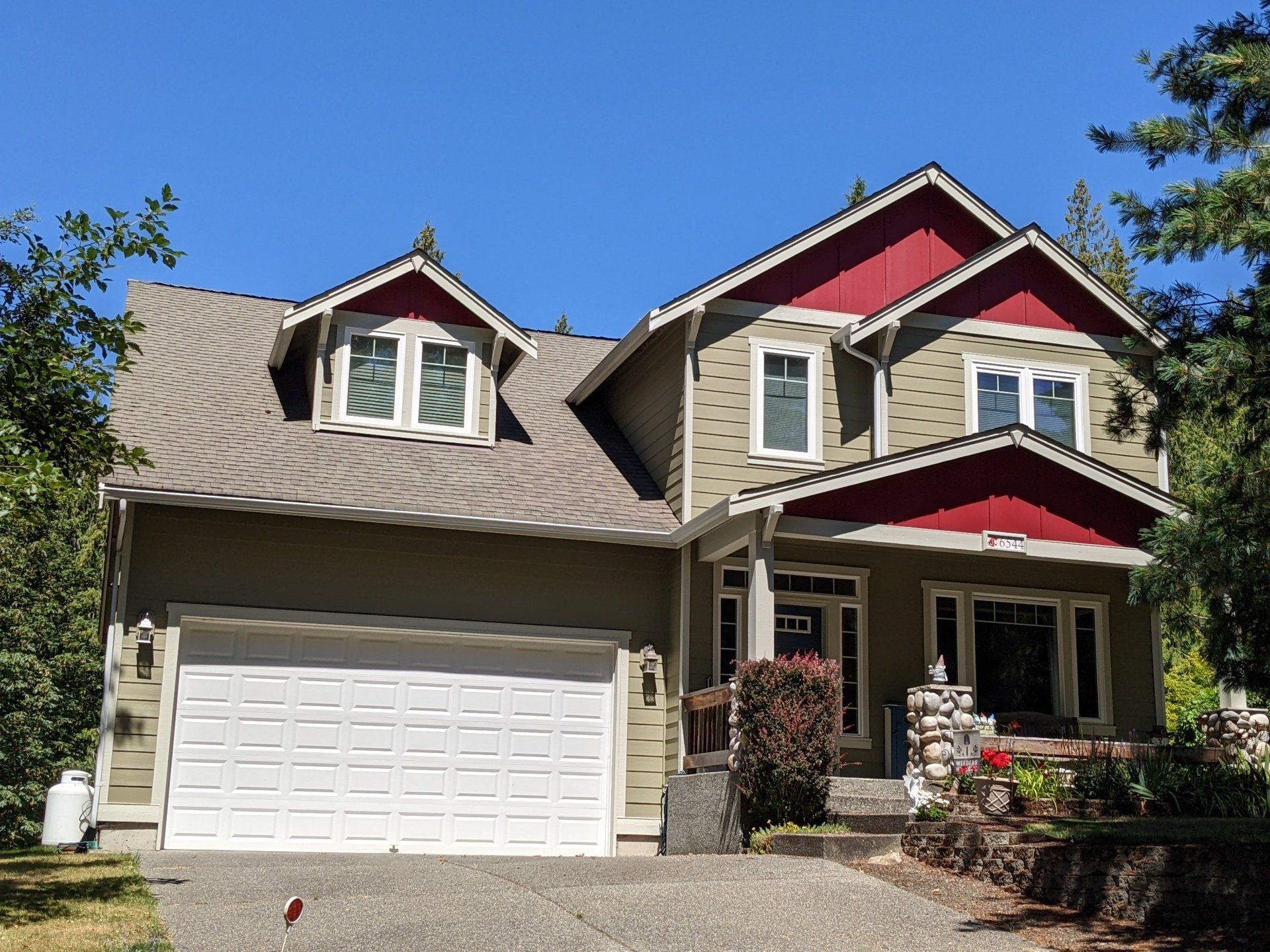 
Front of house with olive green siding, white trim around the windows, and red-painted gable ends and dormer accent.