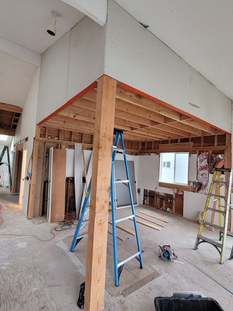 Renovation site with exposed wooden framing, ladders, and drywall in an unfinished room
