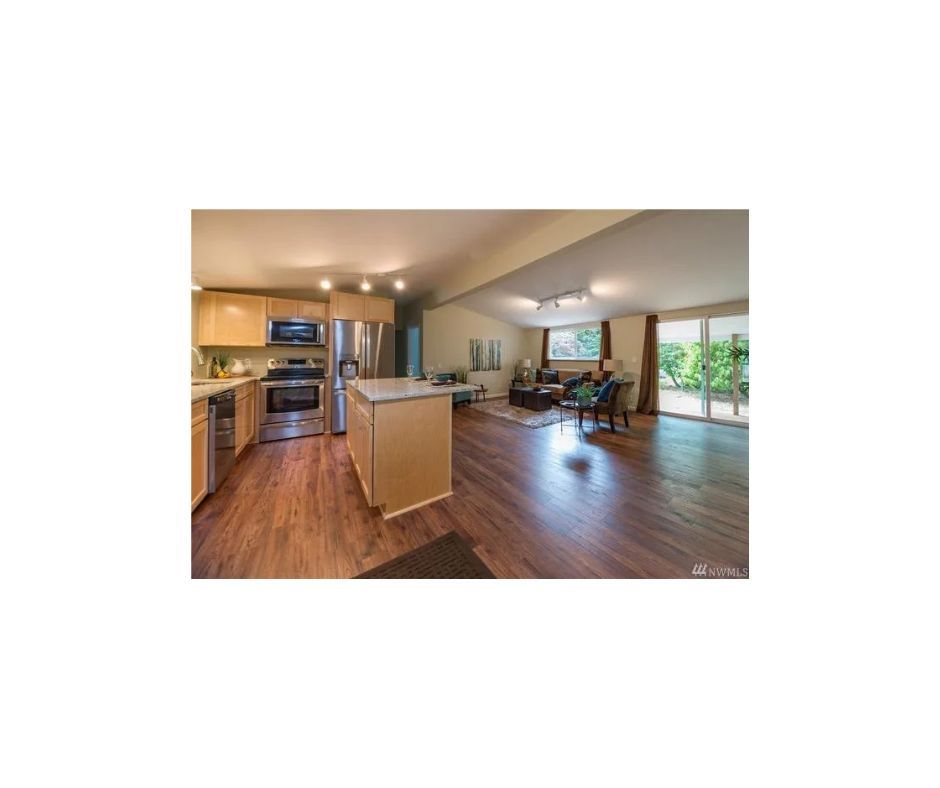 An open kitchen, living and dining room area finished with fresh beige paint, laminate flooring and stainless appliances .