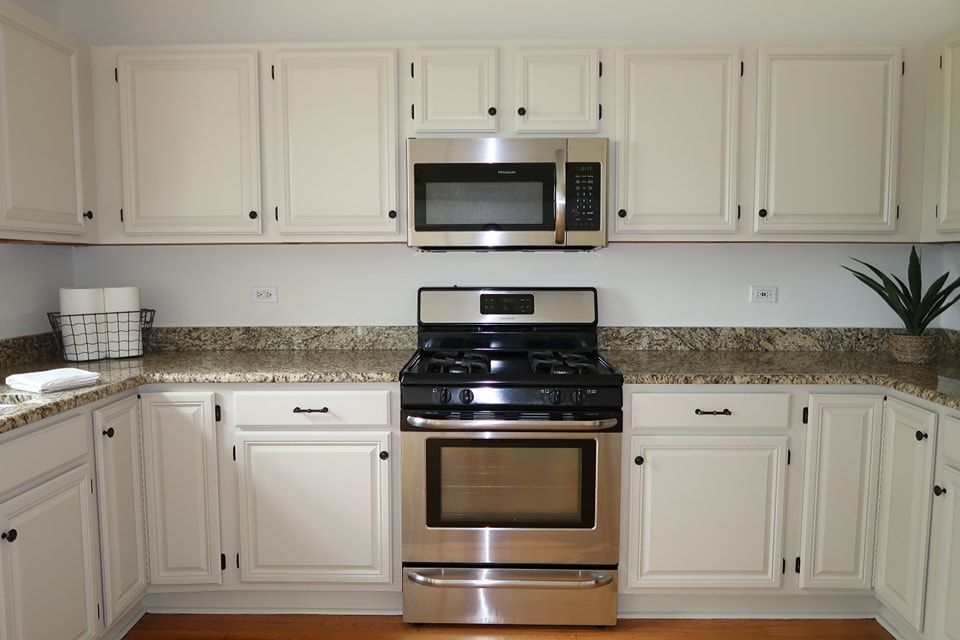 Freshly-painted white kitchen cabinets with a stainless steel oven and microwave and granite countertops.
