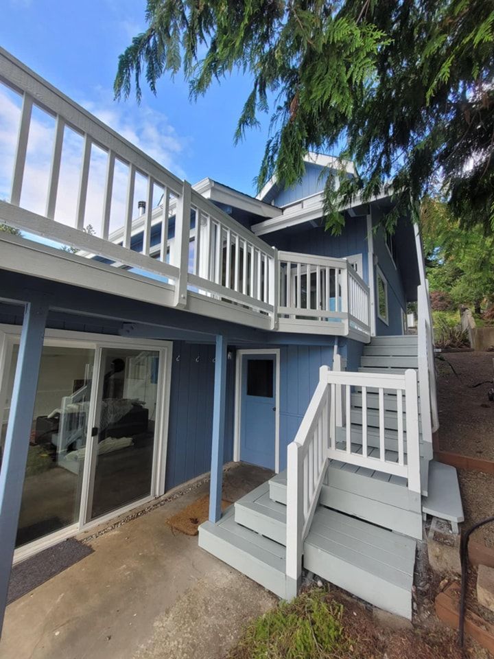 An angled view of blue house with white railing along a second-story deck and stairs.