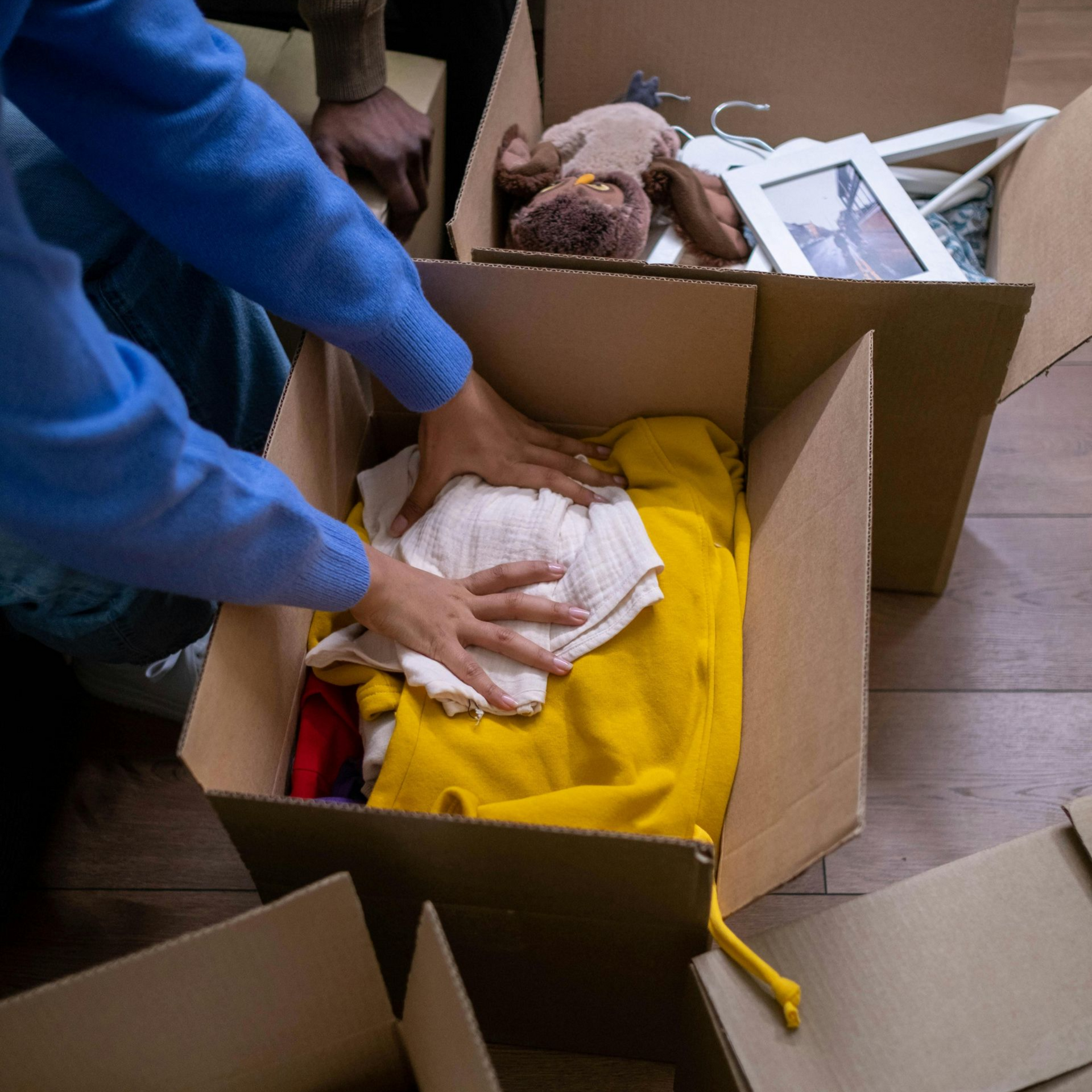 People packing boxes, with clothes, a ukulele, and other items visible.