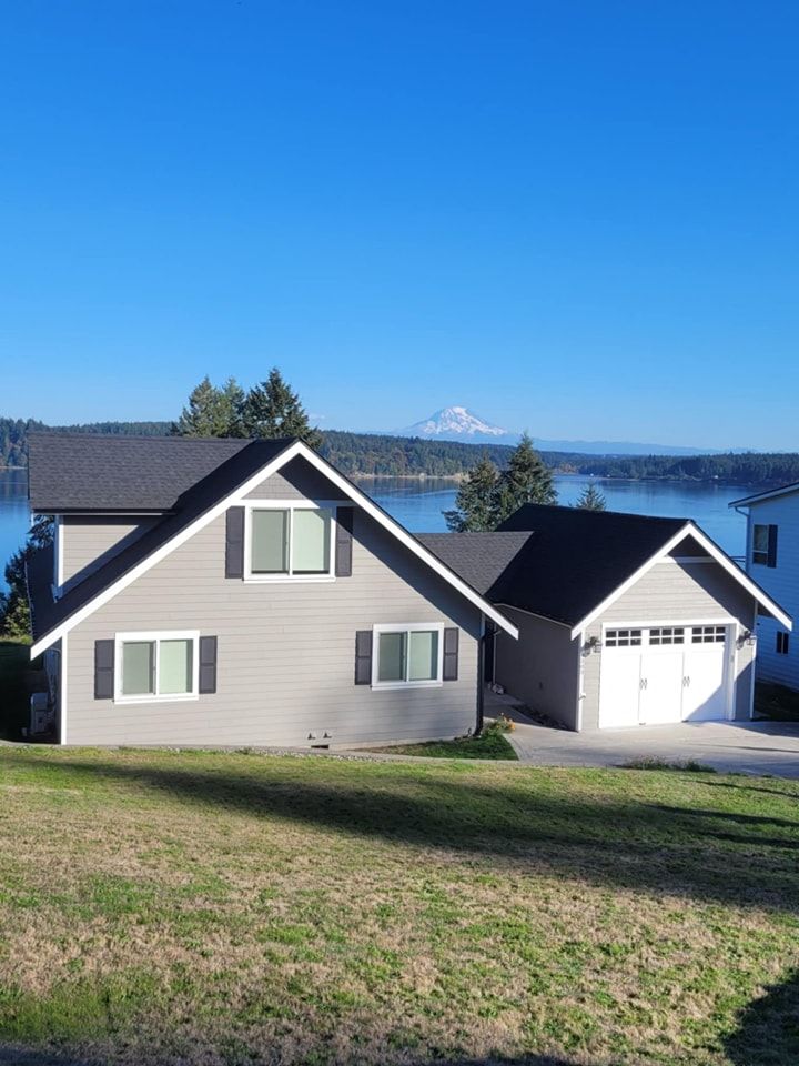 A freshly-painted grey house and matching garage with a white door against a Puget Sound backdrop and Mt. Rainier in the back. 