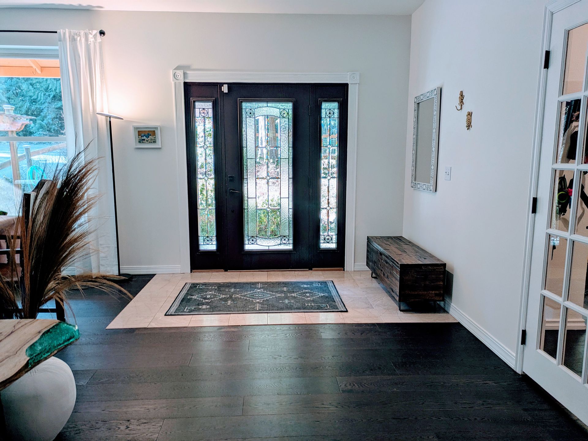 A brightly lit entryway with dark wood floors, light cream walls, and a dark double door with glass.