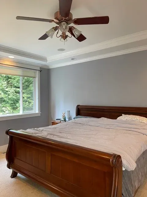 A master bedroom with newly painted gray walls, white trim, a tray ceiling, and a ceiling fan. 