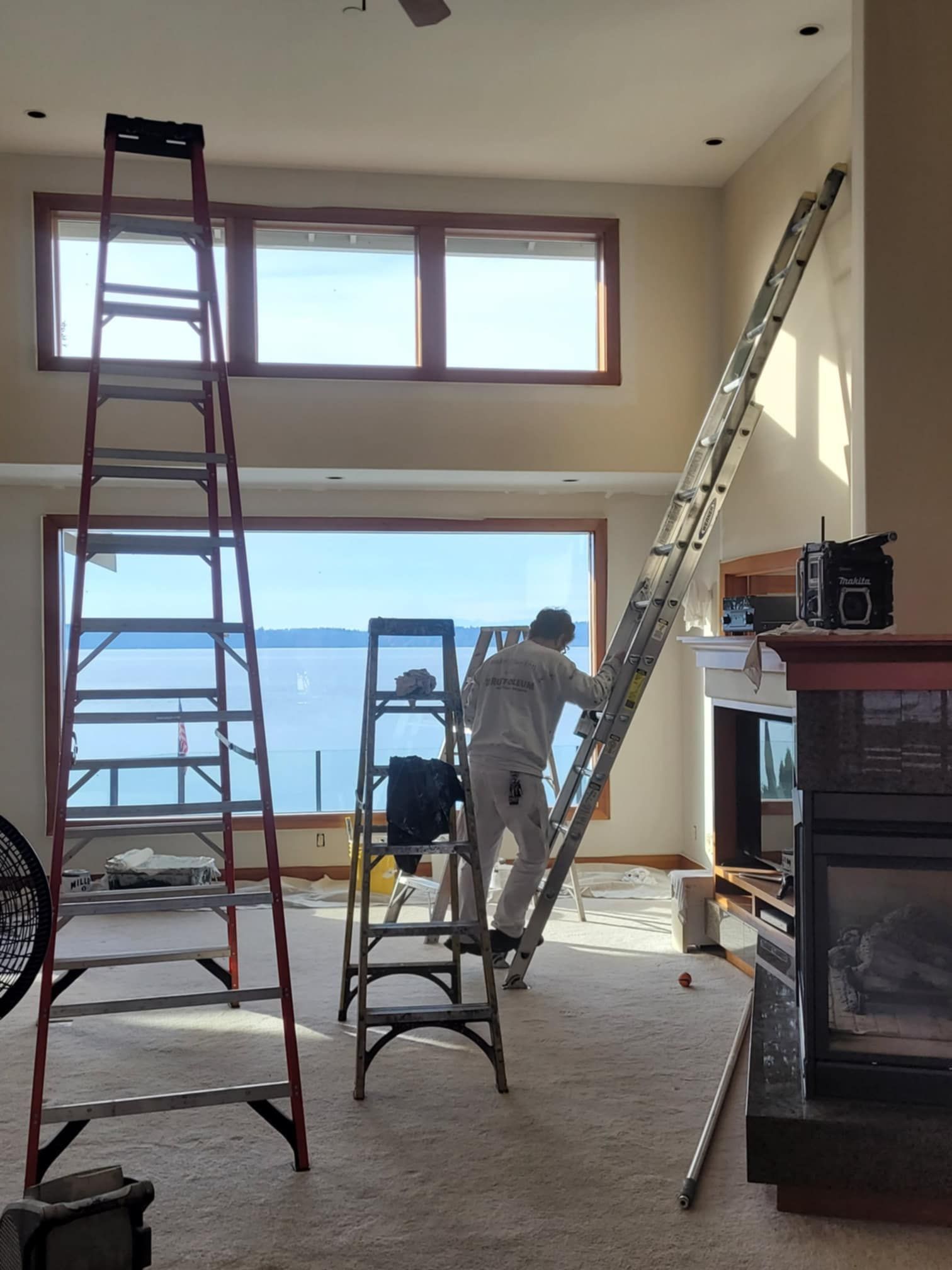 A professional painting contractor sets up ladders to access every corner of a vaulted living room.