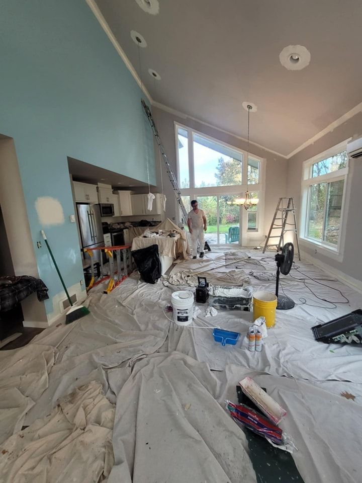 A painter walks thorugh a half-painted kitchen and living room with painting cloths on the floor and work equipment set out.
