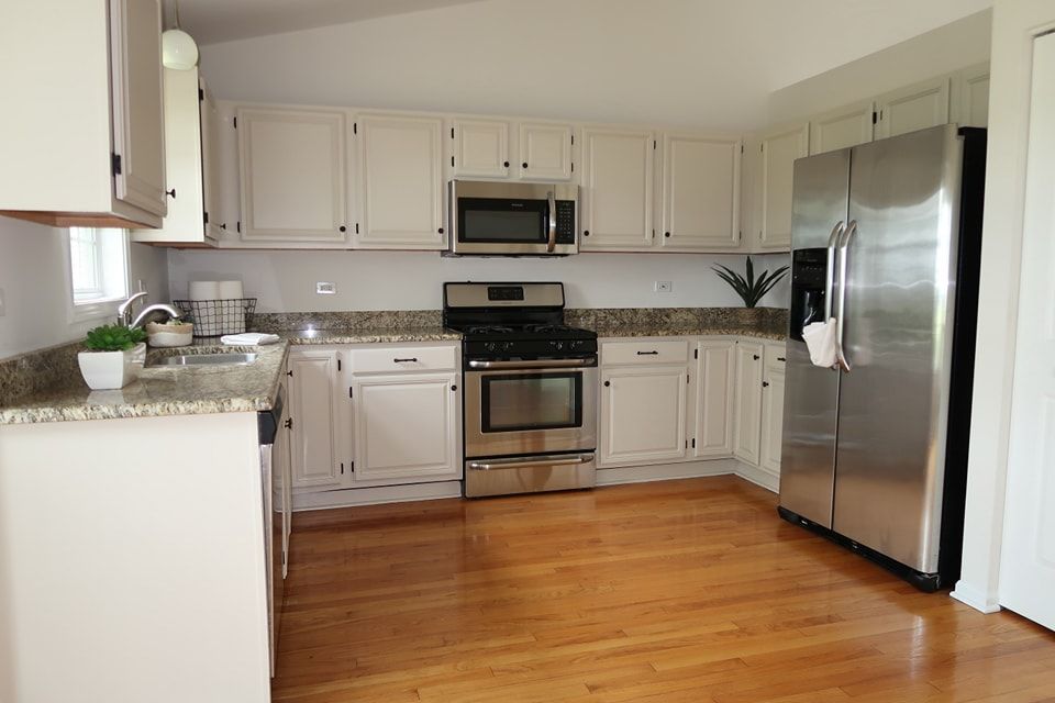 Newly painted white kitchen cabinets are paired with stainless steel appliances and a granite countertop.
