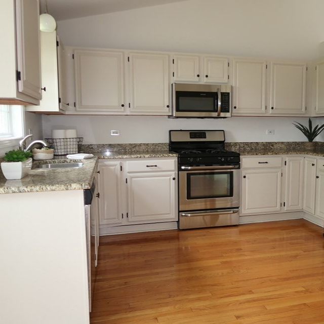 Bright modern kitchen with white cabinets, stainless steel appliances, granite counters, and hardwood floor